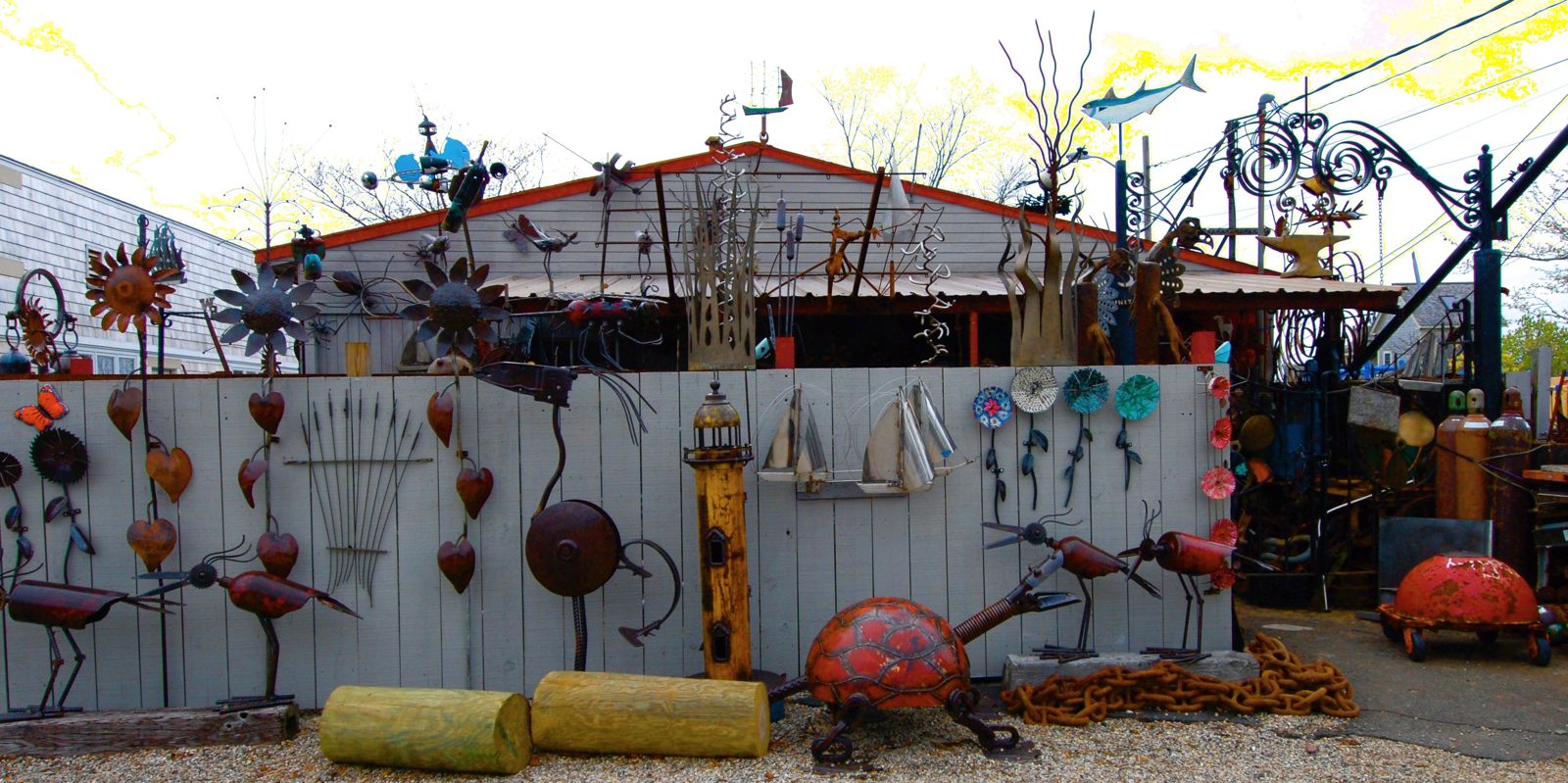 Metal sculptures of birds, sunflowers, and a turtle along the studio fence